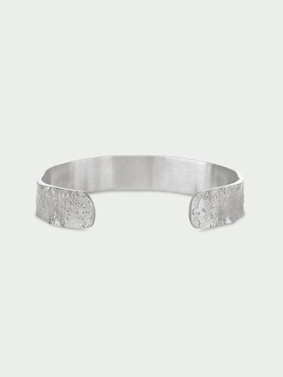 Tutti & Co Solstice Bangle in Silver A wide silver cuff bracelet with a brushed metallic interior and textured, hammered edges, shown on a light gray background.