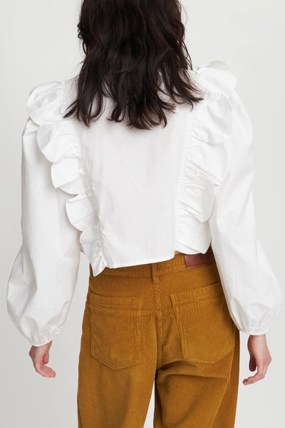 Stella Nova Blouse in white, featuring delicate embroideries on the front. This blouse boasts a round, slightly high neck with scallops and a button closure for a polished touch. Its long sleeves with elastic cuffs and short length make it both comfortable and stylish. Complete with big scallops on the chest and back for added elegance.