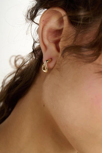 Close-up of a person wearing a gold hoop earring with a neutral background