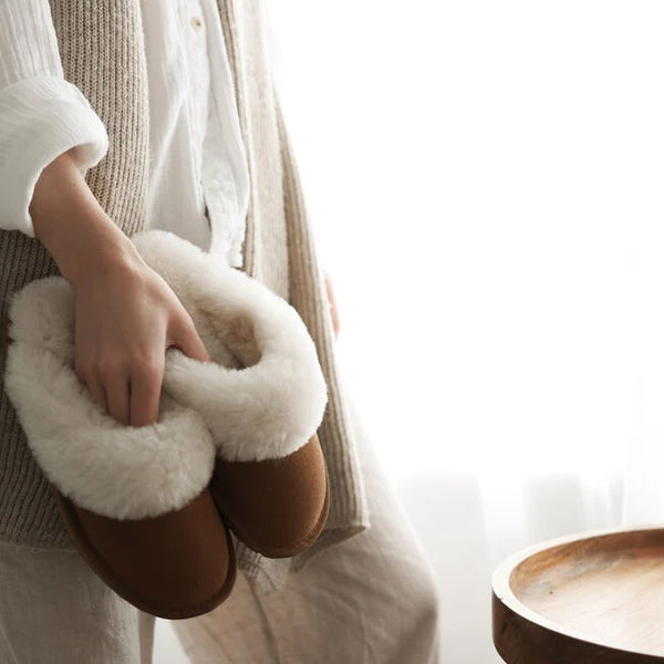 Emu Australia Jolie in Chestnut W10015 Person holding a pair of brown slippers with white fur trim indoors.