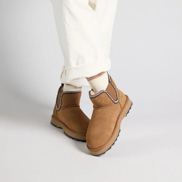 Emu Australia Higgie in Chestnut W13198 Brown suede boots with decorative trim worn with white pants on a light gray background