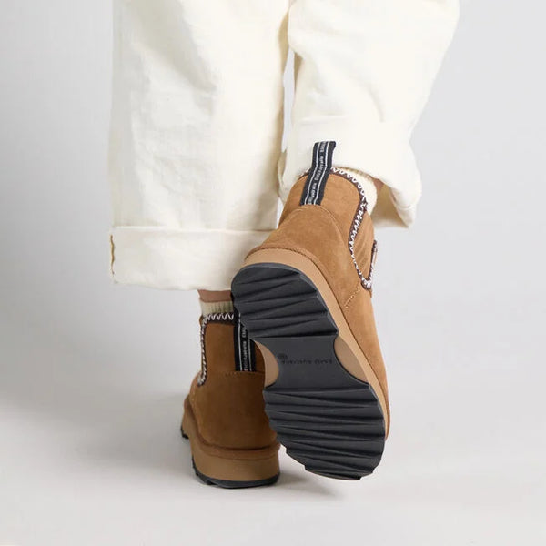 Emu Australia Higgie in Chestnut W13198 Brown slip-on shoes with black soles worn with white pants on a light gray background