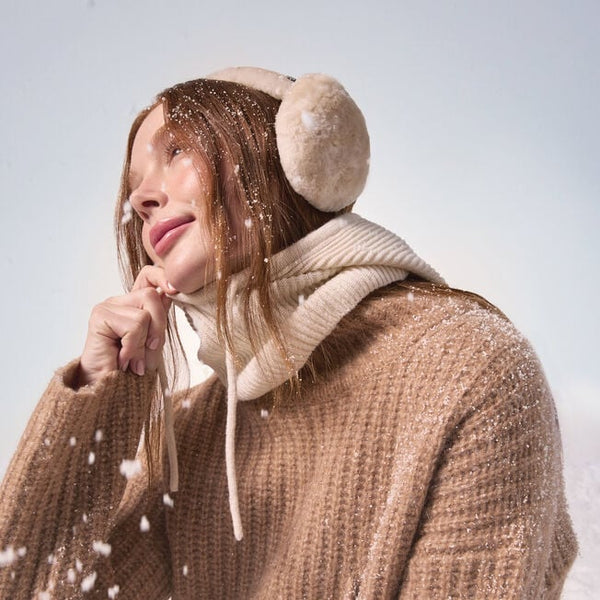 Emu Australia Angahook Earmuffs in Chestnut W9403 Person wearing a beige knitted sweater, scarf, and earmuffs in a snowy setting.