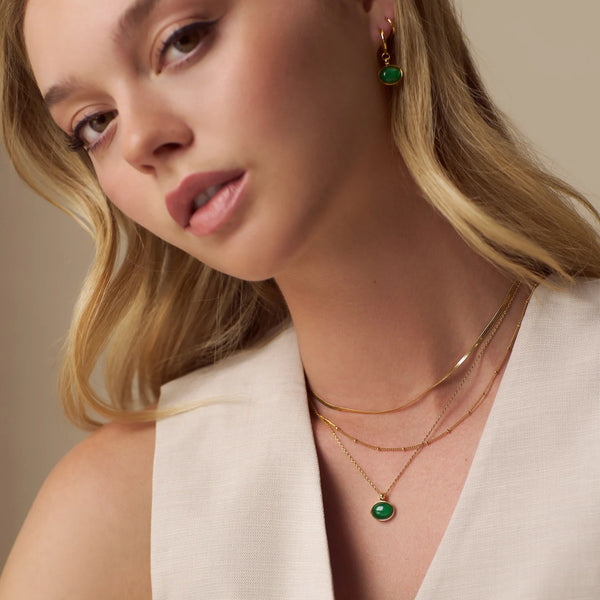 Orelia Semi-Precious Green Jade Pendant Necklace Close-up of a woman wearing gold necklaces and emerald green earrings against a neutral background
