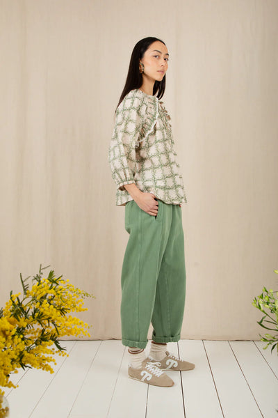 Bonte Florette Top in Clover Woman wearing a green checkered top and green pants standing in a room with a beige wall and white floor.